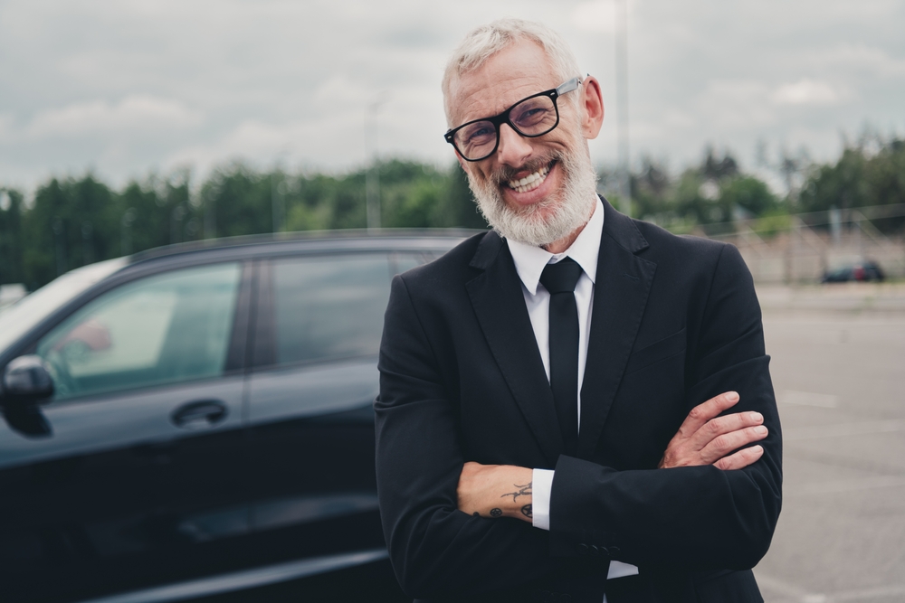 Confident senior businessman in suit standing outside near car